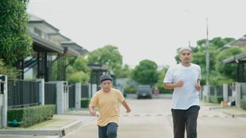uomo asiatico di mezza età musulmano e suo figlio che si divertono a fare jogging nel suo villaggio la sera video