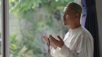 A middle-aged Asian Muslim man prays at his home