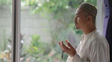 A middle-aged Asian Muslim man prays at his home video