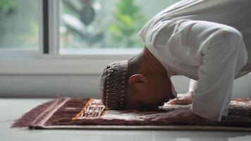 A middle-aged Asian Muslim man prays at his home video
