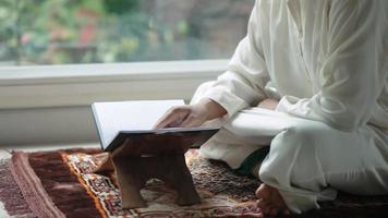 Aziatische moslim man van middelbare leeftijd die thuis de koran zit te lezen video