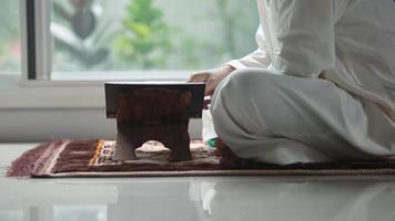 homme d'âge moyen musulman asiatique assis et lisant le coran à son domicile