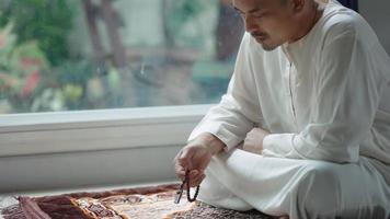 Asian Muslim middle-aged man sitting and reading the Qur'an at his home video
