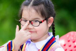 Disparo en la cabeza de niños lindos que usan anteojos debido a la miopía o astigmatismo leve. los niños en edad escolar usan su dedo índice para empujar los anteojos hasta que se ajusten al nivel de los ojos o apretarlos. la niña tiene 6 años. foto