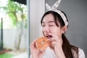 Happy Asian young woman is deliciously biting at a sweet donut.