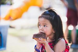 una linda chica asiática de 4-5 años está comiendo un delicioso bollo de chocolate. foto