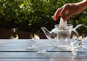 older people put tea bag into glass kettle to make hot afternoon tea in garden photo