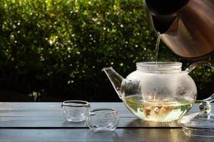 picture of people pouring hot water into clear glass kettle to make tea in afternoon in garden photo