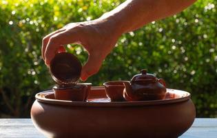 people pouring hot water on set of small kettle and cup to warm them before making chinese traditional tea in garden photo