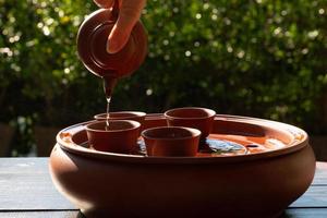picture of people pouring chinese tea from small kettle into cup that is placed on table in garden