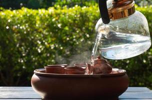 people pouring hot water on set of small kettle and cup to warm them before making chinese traditional tea in garden photo