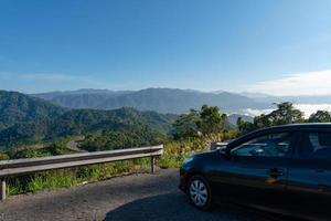 Coche negro estacionado en el lado de la carretera con hermosas montañas verdes y un valle en la mañana