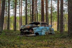 Old blue car wreck standing in a forest in Sweden photo