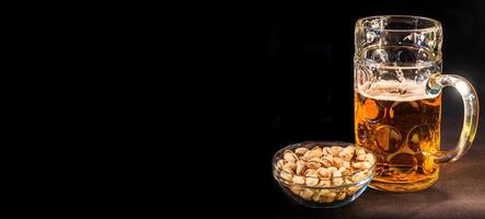 Banner with traditional Octoberfest Bavarian beer in a big one liter mug half drunk with wet walls and pistachios, Germany, at black background with copy space for text. photo
