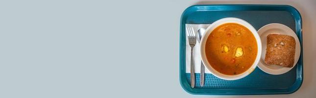 Banner with delicious and appetizing soup with vegetables, tomato and meat, homemade bread, served at a tray with fork and spoon with light blue smooth background for copy space text, details photo