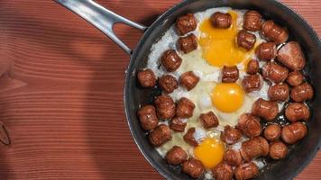 Banner with fried sausages with chicken eggs in process of frying in a frying pan at the red wood table with copy space for text. photo