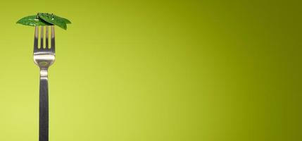 Banner with green fresh leaves picked by a fork for eating as new vegan food isolated at green smooth gradient background with copy space for text, closeup, details photo