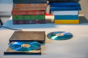 Compact stylish video player for CD and DVD disks with a pile of many TV series movie discs in background. photo