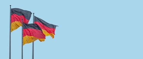 Banner with three national black red yellow flags of Germany in wind and at blue sky background with copy space, details, closeup. Concept of nationality, citizenship and patriotism. photo