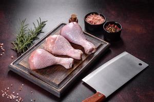 Fresh raw chicken legs with spices, salt and herbs on a cutting board photo