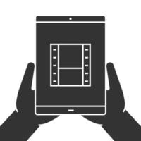 Hands holding tablet computer glyph icon. Watching films. Silhouette symbol. Tablet computer with video tape. Negative space. Vector isolated illustration