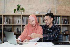 dos jóvenes compañeros de empresas emergentes, personas que son parejas islámicas, hablan con una sonrisa sobre el éxito trabajando en un negocio de comercio electrónico. Utilice la computadora portátil para comunicarse en línea a través de Internet en una oficina pequeña. foto