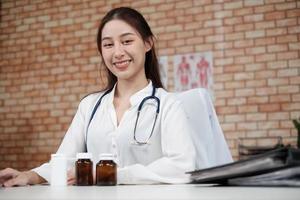 Retrato de hermosa doctora de origen asiático en camisa blanca con estetoscopio, sonriendo y mirando a la cámara en la clínica del hospital. una persona que tenga experiencia en tratamiento profesional. foto