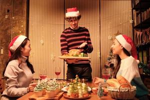 comida especial de la familia, el joven sirve pavo asado a los amigos, alegre con bebidas y disfruta comiendo, cena en el comedor de la casa decorado para el festival de navidad y la fiesta de las celebraciones de año nuevo. foto