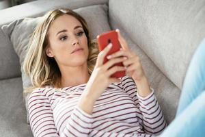 Young blonde woman using her smartphone lying on the sofa. photo