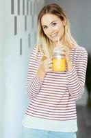 mujer sonriente bebiendo un vaso de jugo de naranja natural en casa. foto