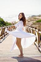 Young woman wearing a beautiful white dress in Spanish fashion on a boardwalk on the beach.