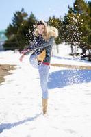 Joven mujer feliz pateando nieve en un bosque cubierto de nieve en las montañas foto