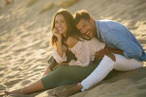 Pareja joven riendo juntos sentados en la arena de la playa foto