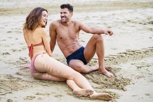 Young couple sitting together on the sand of the beach photo