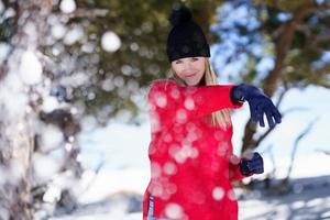 Blonde woman throwing snowballs forward in a snow-covered forest in the mountains photo