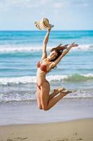 mujer joven con hermoso cuerpo en traje de baño saltando en una playa tropical.