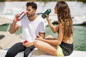 Young sporting couple hydrate themselves with water in metal cans while taking a break after sport. photo