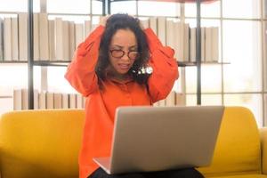 Mujer latina que trabaja con el portátil en el sofá con sentimiento estresado