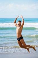 joven con hermoso cuerpo en traje de baño saltando en una playa tropical. foto