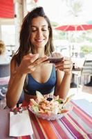 Mujer joven fotografiando su ensalada con un teléfono inteligente mientras está sentado en un restaurante foto