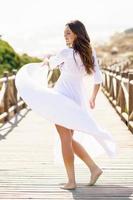 Young woman wearing a beautiful white dress in Spanish fashion on a boardwalk on the beach.