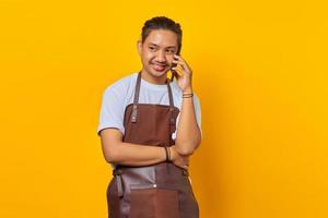 Portrait of cheerful young Asian woman receiving incoming call on smartphone and looking at camera on yellow background photo