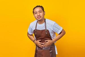 Portrait of Asian young man wearing apron Showing Hands on stomach due to nausea, painful illness feeling unwell photo