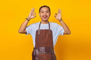 Cheerful handsome young barista showing ok gesture isolated on yellow background photo