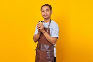 Portrait of cheerful positive handsome man holding paper cup and looking ahead isolated on yellow background photo