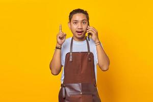 Portrait of surprised asian young man talking on smartphone and finger pointing up. yellow background photo