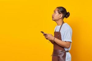 Portrait of happy young Asian man using smartphone and looking at empty space on yellow background photo