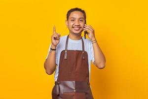 Portrait of smiling Asian young man talking on smartphone and finger pointing up. yellow background photo