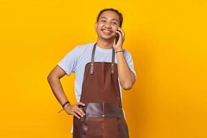 Retrato de sonriente y alegre joven asiático hablando por teléfono inteligente sobre fondo amarillo foto