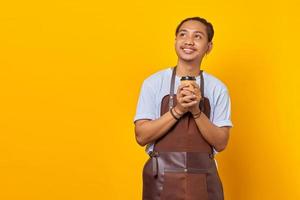 Portrait of cheerful positive handsome man holding paper cup and looking sideways over yellow background photo